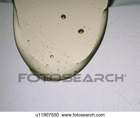 Stock Image - Light Yellow Colered Viscous Liquid Being Pured Into Another Liquid, Front View. Fotosearch