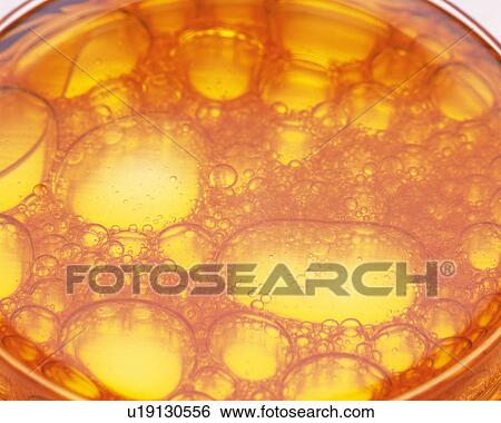 Stock Photograph - Orange Oil in a Flat Glass Bin, Containing a Lot of Bubbles, High Angle View. Fotosearch