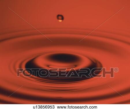 Stock Image - Red-colored Oil, a Drop Falling on the Surface, High Angle View. Fotosearch