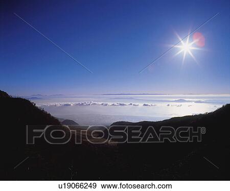 Stock Photo -  a Sea of Clouds Surrounded By Mountains Under the Shining Sun, High Angle View, Lens Flare. Fotosearch