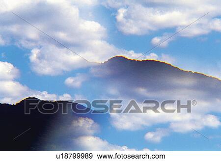 Stock Photo -  Several Mountains and Clouds Overlapping Under a Blue Sky, Low Angle View. Fotosearch