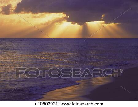 Stock Image -  Several Sunbeams Shining Through Some Clouds With a Beach in Front, Side View. Fotosearch