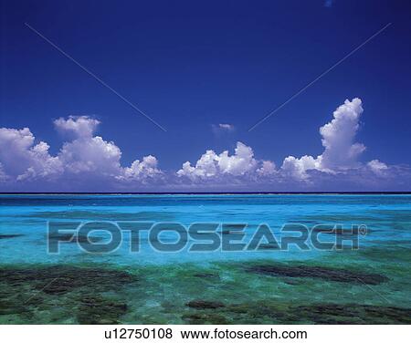 Stock Photo -  the Ocean With Transparent Water, Under a Blue Sky and Several Clouds, Front View. Fotosearch
