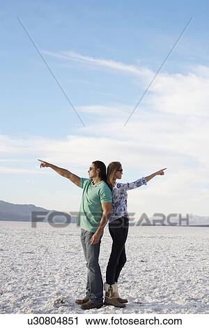 Couple standing back to back and pointing to opposite directions in desert View Large Photo Image Stock Image - Couple standing back to back and pointing to opposite directions in desert. Fotosearch