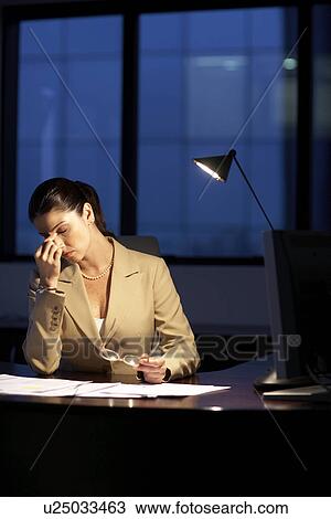 Stock Image - Female office worker working late. Fotosearch