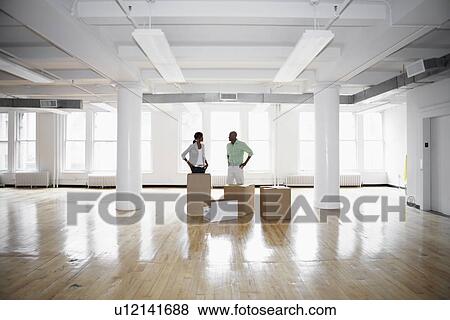 Man and woman standing by boxes in empty office View Large Photo Image Stock Photo - Man and woman standing by boxes in empty office. Fotosearch