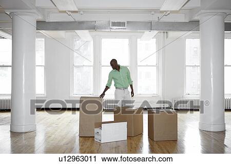Stock Image - Man unpacking boxes in empty office. Fotosearch