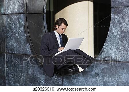 Stock Image - Mid Adult Businessman Using Laptop on Circular Window. Fotosearch