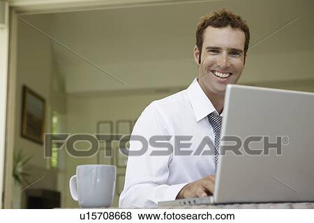 Stock Photo - Mid adult man using laptop in living room (low angle view). Fotosearch