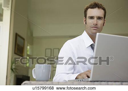 Stock Photo - Mid adult man using laptop in living room (low angle view). Fotosearch