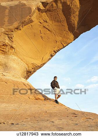 Hiker walking under arched rock View Large Photo Image Stock Image - Hiker walking under arched rock. Fotosearch