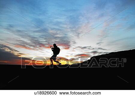 Stock Image - Male Hiker Playing Bugle on Car Roof at Sunset. Fotosearch