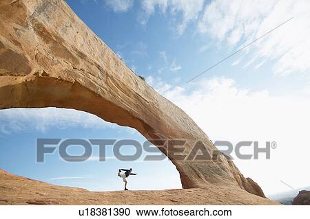 Stock Image - Man stretching under arched rock. Fotosearch