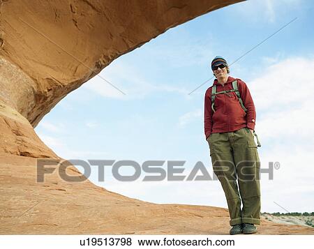 Stock Photo - Young hiker standing on red rock, portrait, low angle view. Fotosearch