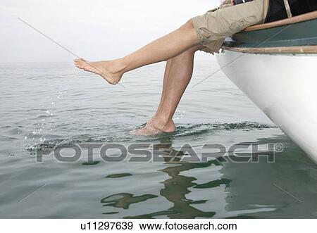 Couple sitting on edge of boat, dipping feet in water (low angle view) View Large Photo Image Stock Photo - Couple sitting on edge of boat, dipping feet in water (low angle view). Fotosearch