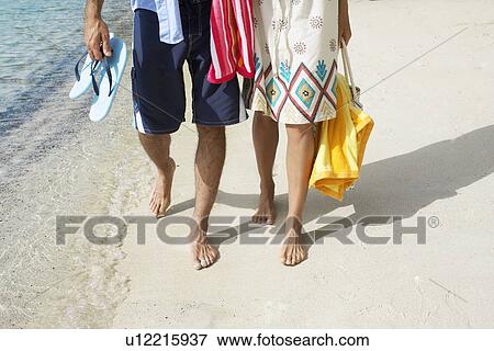 Stock Photo - Couple walking on sandy beach (low section). Fotosearch