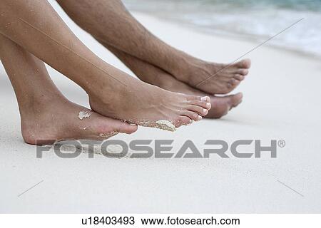 Stock Image - Couple's feet on sandy beach (focus on feet). Fotosearch