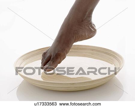 Stock Image - Woman dipping toe in bowl of water (close-up). Fotosearch