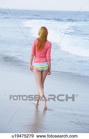 Stock Photo - Woman walking on beach (rear view). Fotosearch