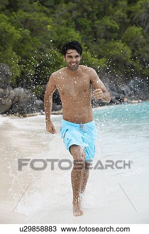 Stock Image - Young man running on sandy beach, St. John, US Virgin Islands, USA. Fotosearch