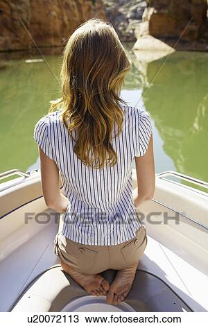 Stock Image - Young woman sitting in boat (rear view). Fotosearch