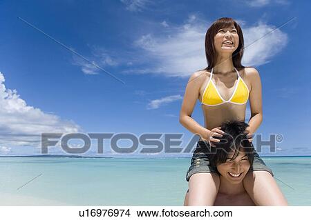 Picture - Man giving woman piggyback ride on beach, smiling, Saipan, USA . Fotosearch