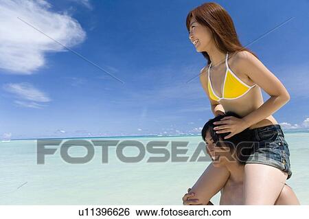 Stock Photograph - Man giving woman piggyback ride on beach, smiling, Saipan, USA . Fotosearch