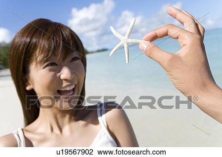 Stock Image - Man showing woman dead starfish, woman smiling, Saipan, USA . Fotosearch