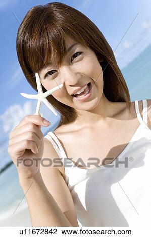 Stock Image - Portrait of a young woman holding a starfish, smiling, Saipan, USA . Fotosearch