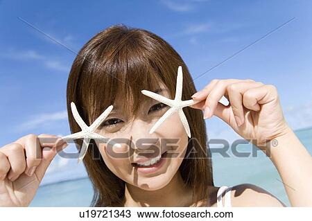 Stock Image - Portrait of a young woman holding starfishes, smiling, Saipan, USA . Fotosearch