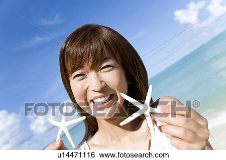 Stock Photograph - Portrait of a young woman holding starfishes, smiling, Saipan, USA . Fotosearch