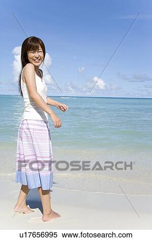 Stock Photography - Portrait of a young woman standing on beach, smiling and looking back, Saipan, USA . Fotosearch