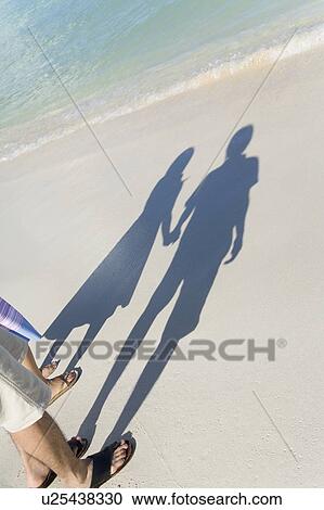 Stock Image - Shadow of young couple standing on beach, hand in hand, Saipan, USA . Fotosearch