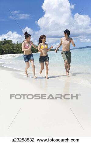 Stock Image - Three young people running on beach, smiling, copy space, Saipan, USA . Fotosearch