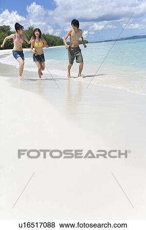 Stock Photo - Three young people running on beach, smiling, copy space, Saipan, USA . Fotosearch
