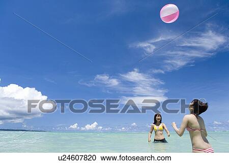 Stock Image - Two young women playing with beach ball, Saipan, USA . Fotosearch