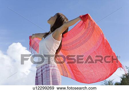 Stock Photo - Woman holding fabric behind back on beach, closing eyes, Saipan, USA . Fotosearch
