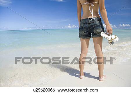 Stock Photography - Woman standing on beach, holding sandals, Saipan, USA . Fotosearch