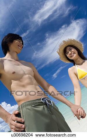 Picture - Young couple smiling on beach, hand in hand, Saipan, USA . Fotosearch