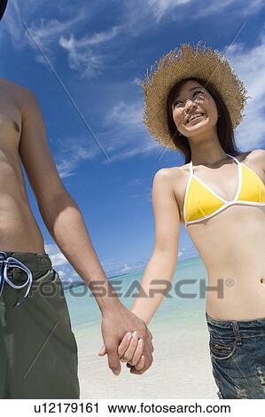 Stock Image - Young couple smiling on beach, hand in hand, Saipan, USA . Fotosearch