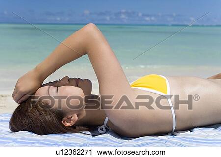 Stock Image - Young woman lying on beach, closing eyes, Saipan, USA . Fotosearch