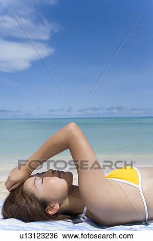 Stock Photograph - Young woman lying on beach, closing eyes, Saipan, USA . Fotosearch