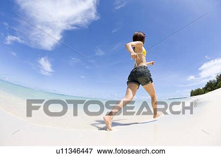 Stock Photo - Young woman running on beach, fish-eye lens, Saipan, USA . Fotosearch