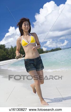 Stock Photo - Young woman running on beach, holding sandals, Saipan, USA . Fotosearch