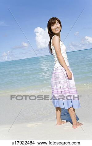 Picture - Young woman standing on beach, smiling and looking back, Saipan, USA . Fotosearch