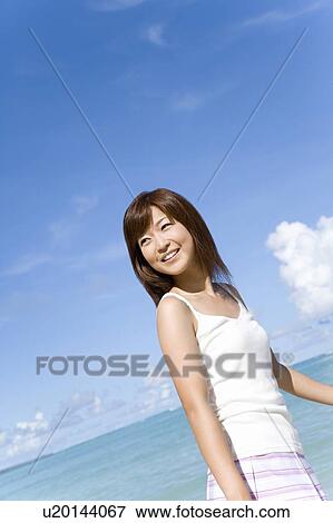 Stock Photo - Young woman standing on beach, smiling and looking back, Saipan, USA . Fotosearch