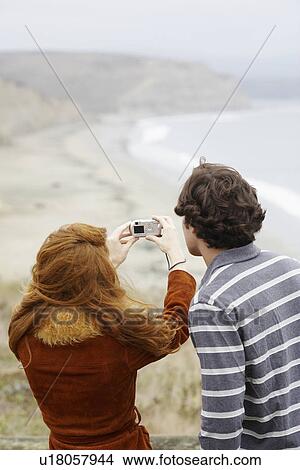 Picture - Couple taking photographs at beach (rear view). Fotosearch
