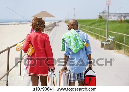 Stock Image - Man and woman carrying picnic equipment at beach (rear view), Spring Lake, New Jersey, USA. Fotosearch