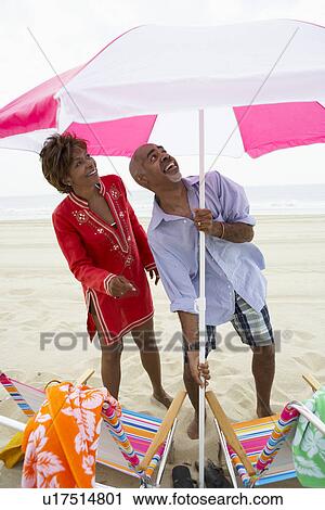 Stock Image - Man and woman setting up beach umbrella. Fotosearch