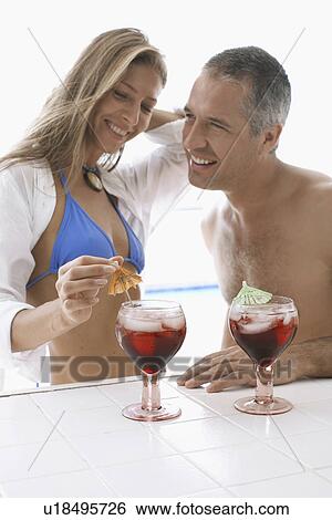 Stock Photograph - Mid adult couple in beach attire having cocktails. Fotosearch